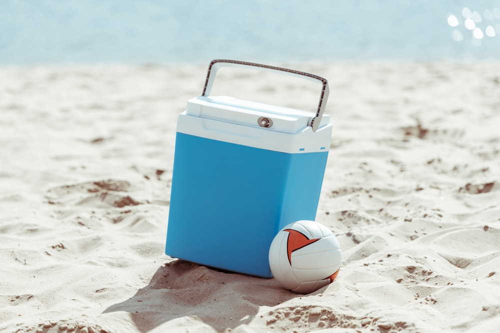 Eine blaue Kühlbox am Strand, daneben ein Volleyball