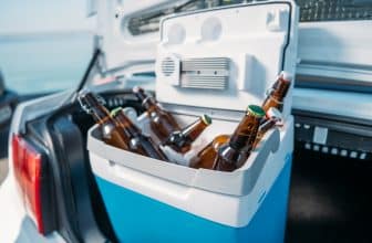 Mit Bierflaschen gefüllte Kühlbox im geöffneten Kofferraum eines Autos.